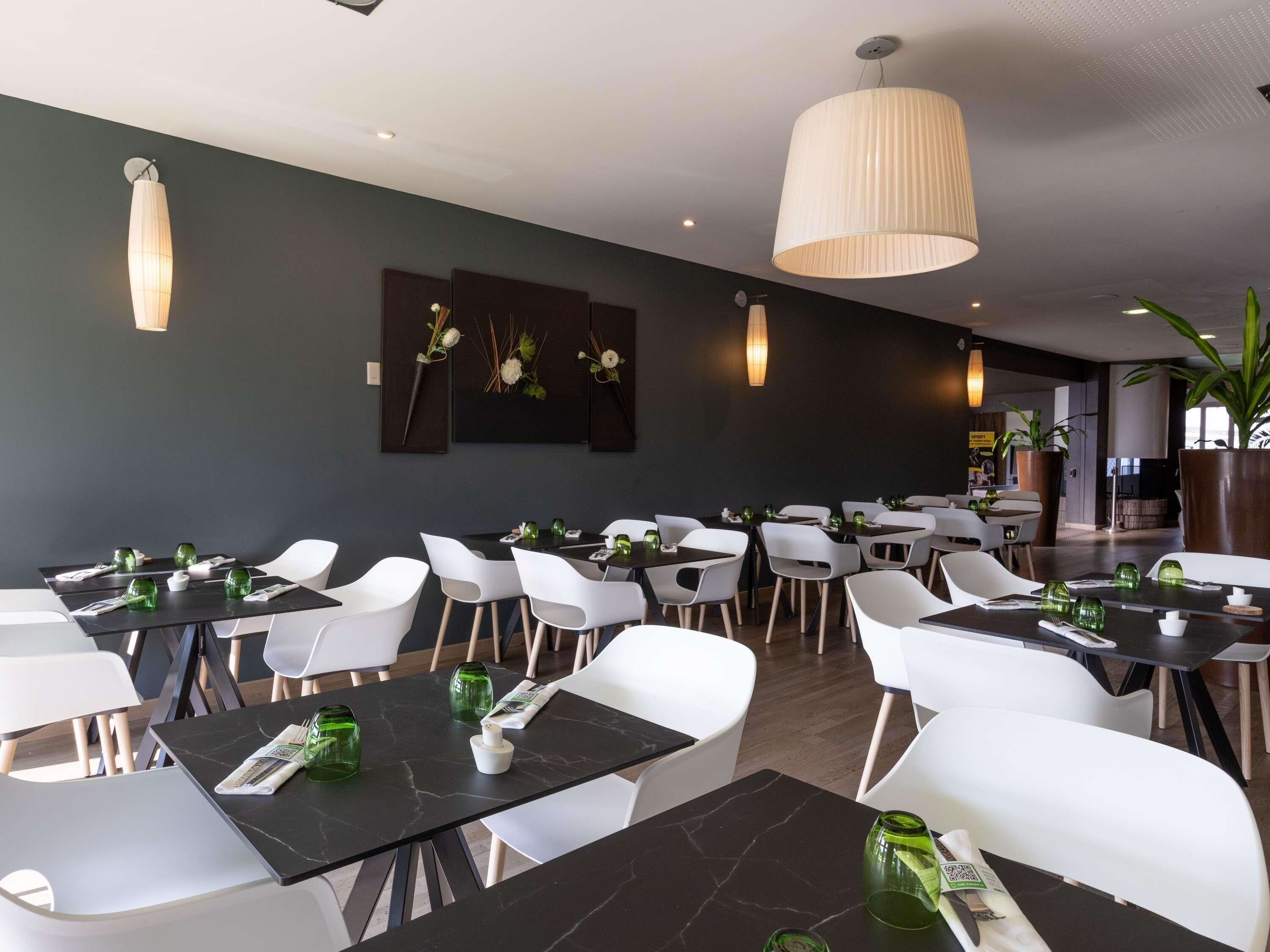 A modern restaurant interior with black marble tables, white chairs, and pendant lighting.