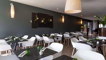 A modern restaurant interior with black marble tables, white chairs, and pendant lighting.