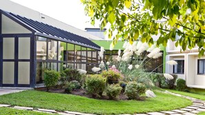 A modern house with a glass conservatory, a well-maintained garden with various plants and flowers, and a stone pathway. - Ibis Styles Chalon sur Saone (Chalon-sur-Saone)