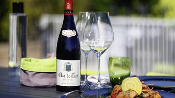 A bottle of Clos de Tart wine, a glass of water, and a plate of food on a table outdoors.