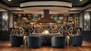 A cozy lounge area with a fireplace, comfortable seating, and a wall adorned with framed landscape paintings. - Graduate by Hilton Minneapolis (Minneapolis)