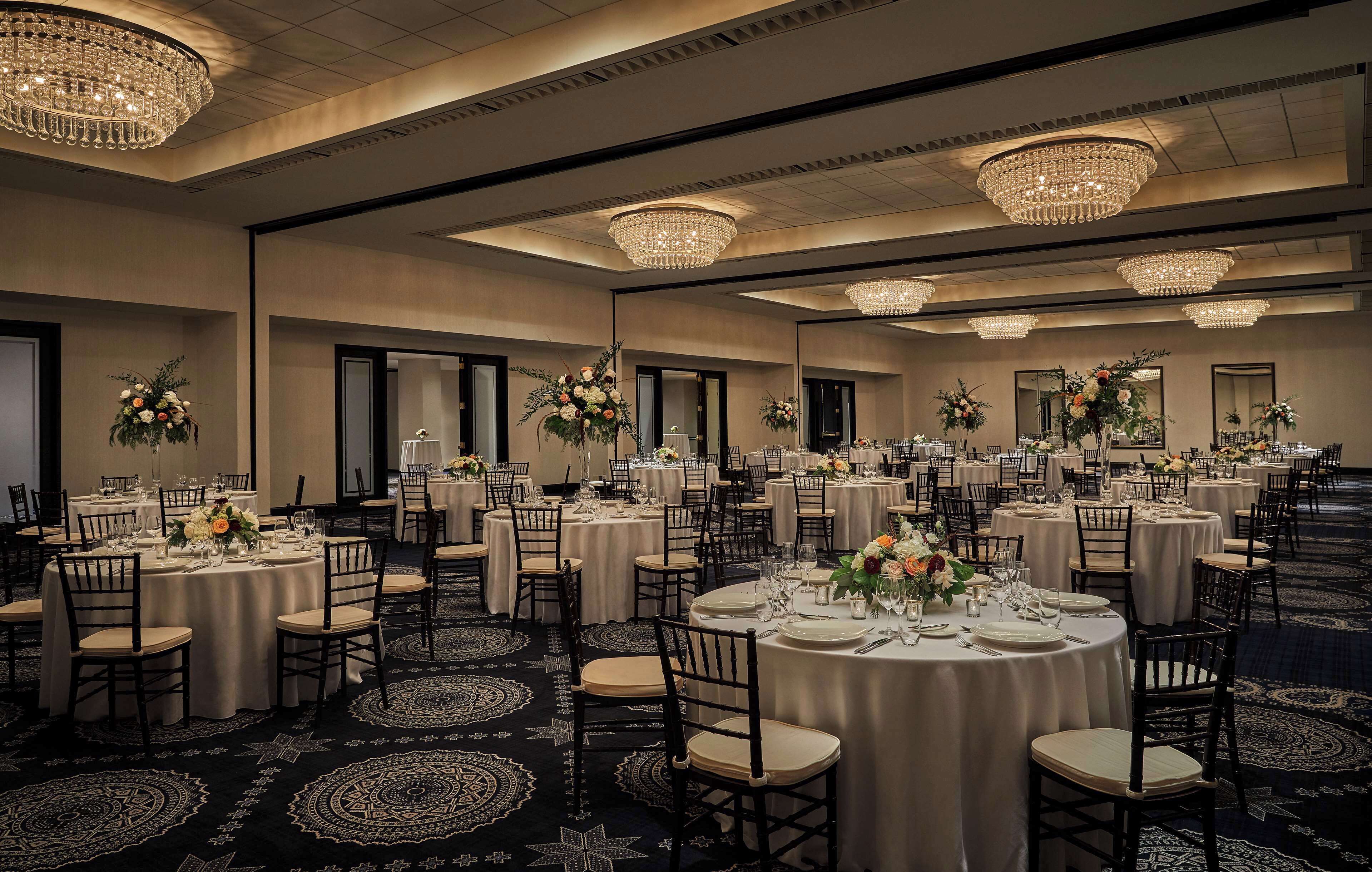 Une salle de banquet avec des tables rondes, des chaises, des lustres et des compositions florales en guise de centre de table.