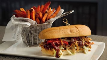 A sandwich with barbecue sauce and a side of sweet potato fries on a white plate.