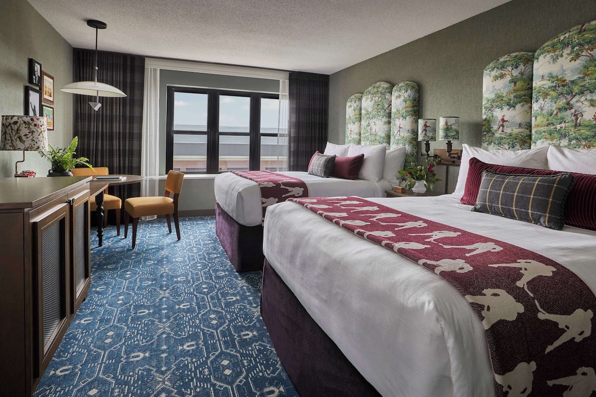 Ein Hotelzimmer mit zwei Betten, einem Schreibtisch, einem Stuhl und einem großen Fenster.