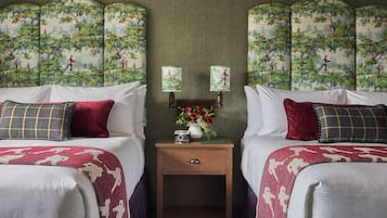 Une chambre d’hôtel avec deux lits, chacun recouvert d’une couvre-lit à motifs rouges et blancs, une petite table de chevet en bois surmontée d’un vase de fleurs et une plante verte.