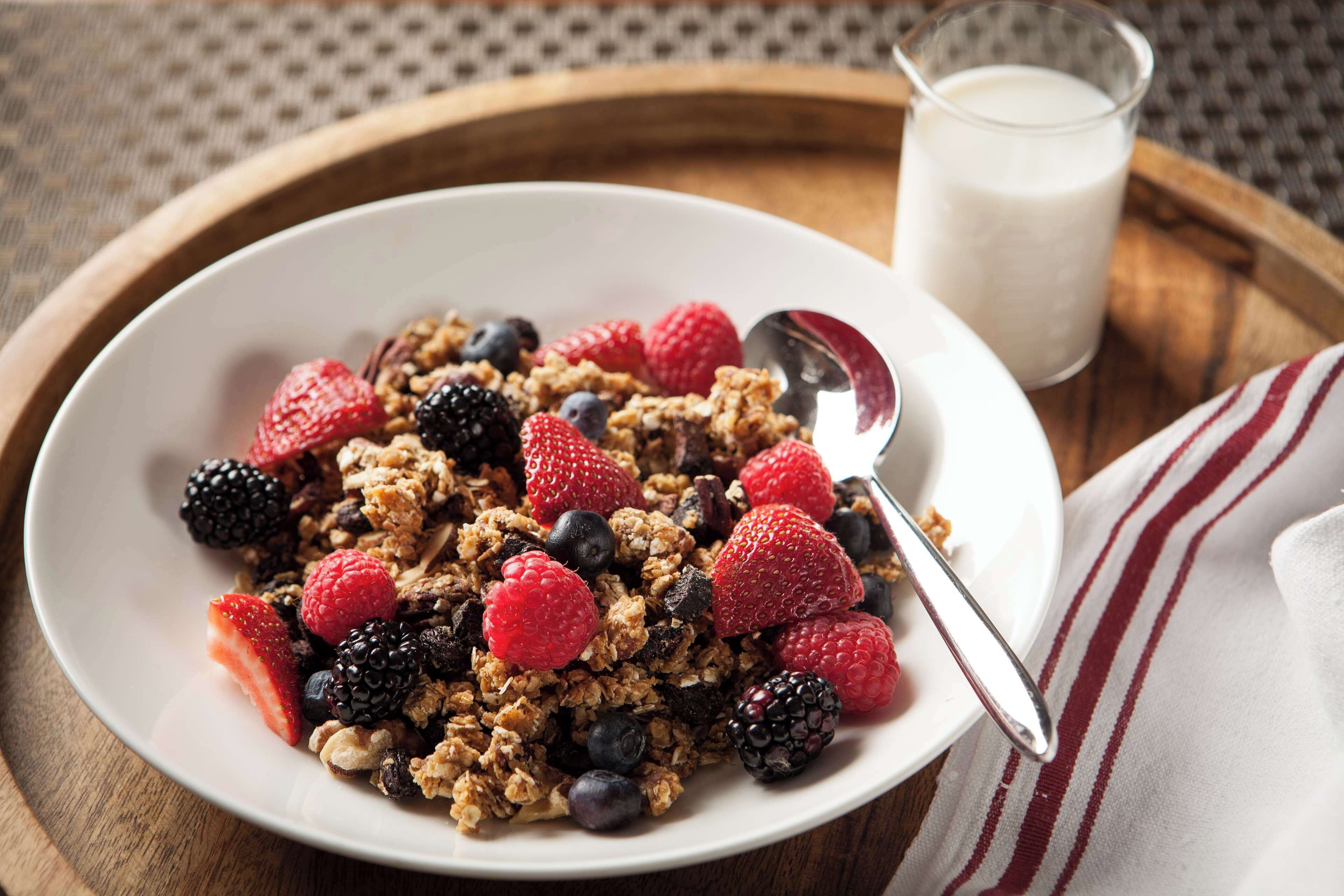A bowl of granola with berries and a glass of milk on a wooden tray.