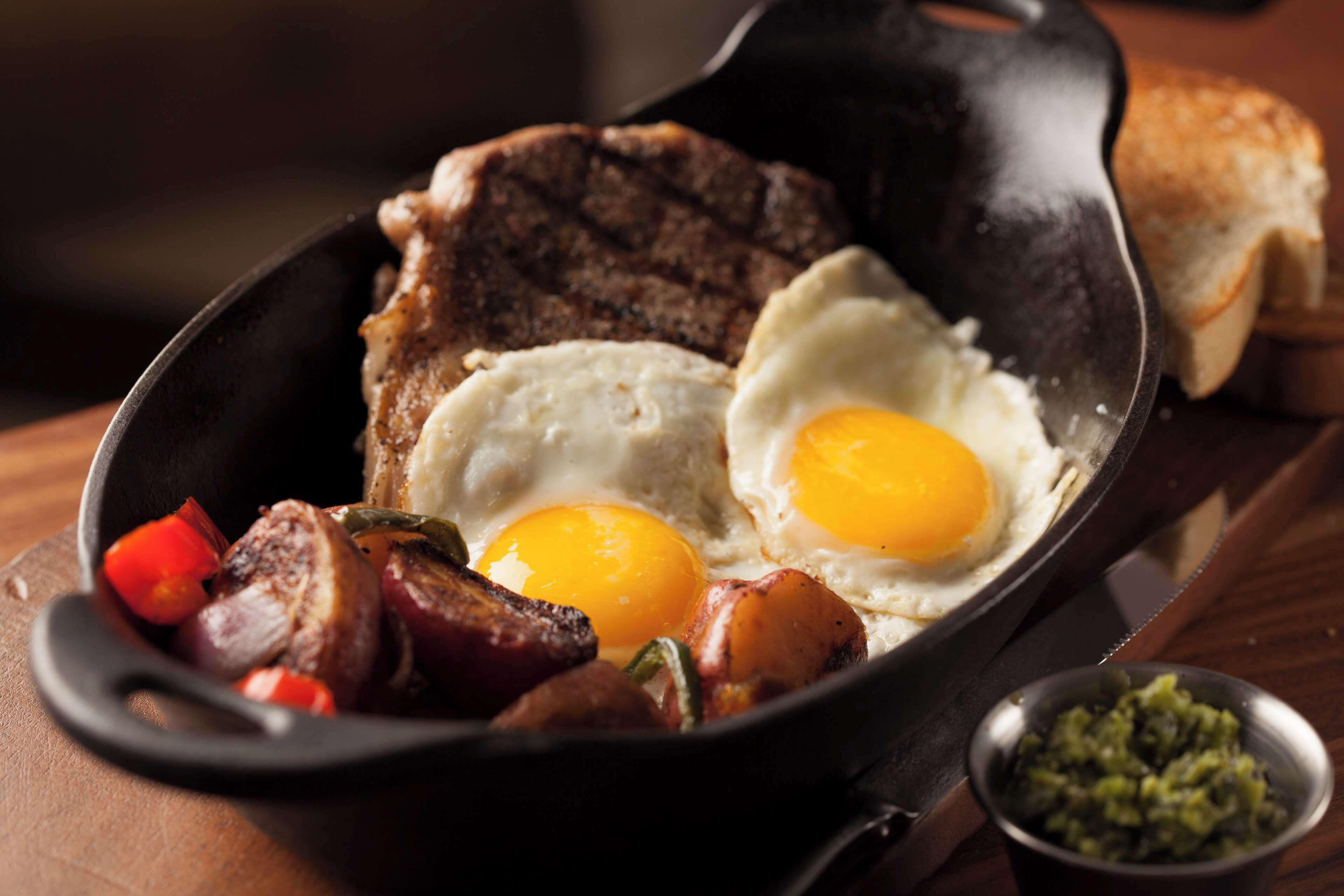 A skillet with eggs, meat, and vegetables.