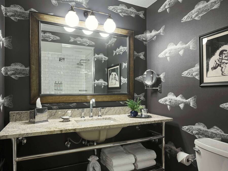 Een badkamer met een grote spiegel, een wastafel en een toilet. De muren zijn versierd met vismotieven.
