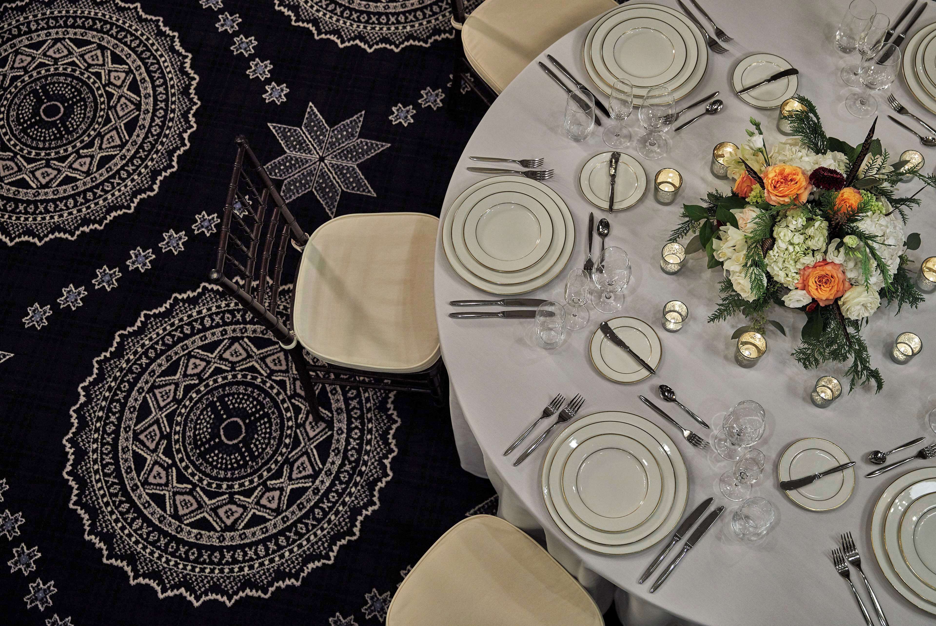 A round table set for a meal with white plates, silverware, and a centerpiece of flowers.