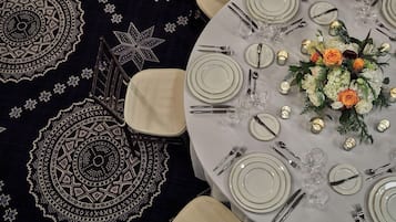 A round table set for a meal with white plates, silverware, and a centerpiece of flowers.