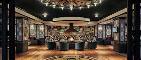 A luxurious lobby with a central fire feature, elegant seating, and a circular emblem on the floor.