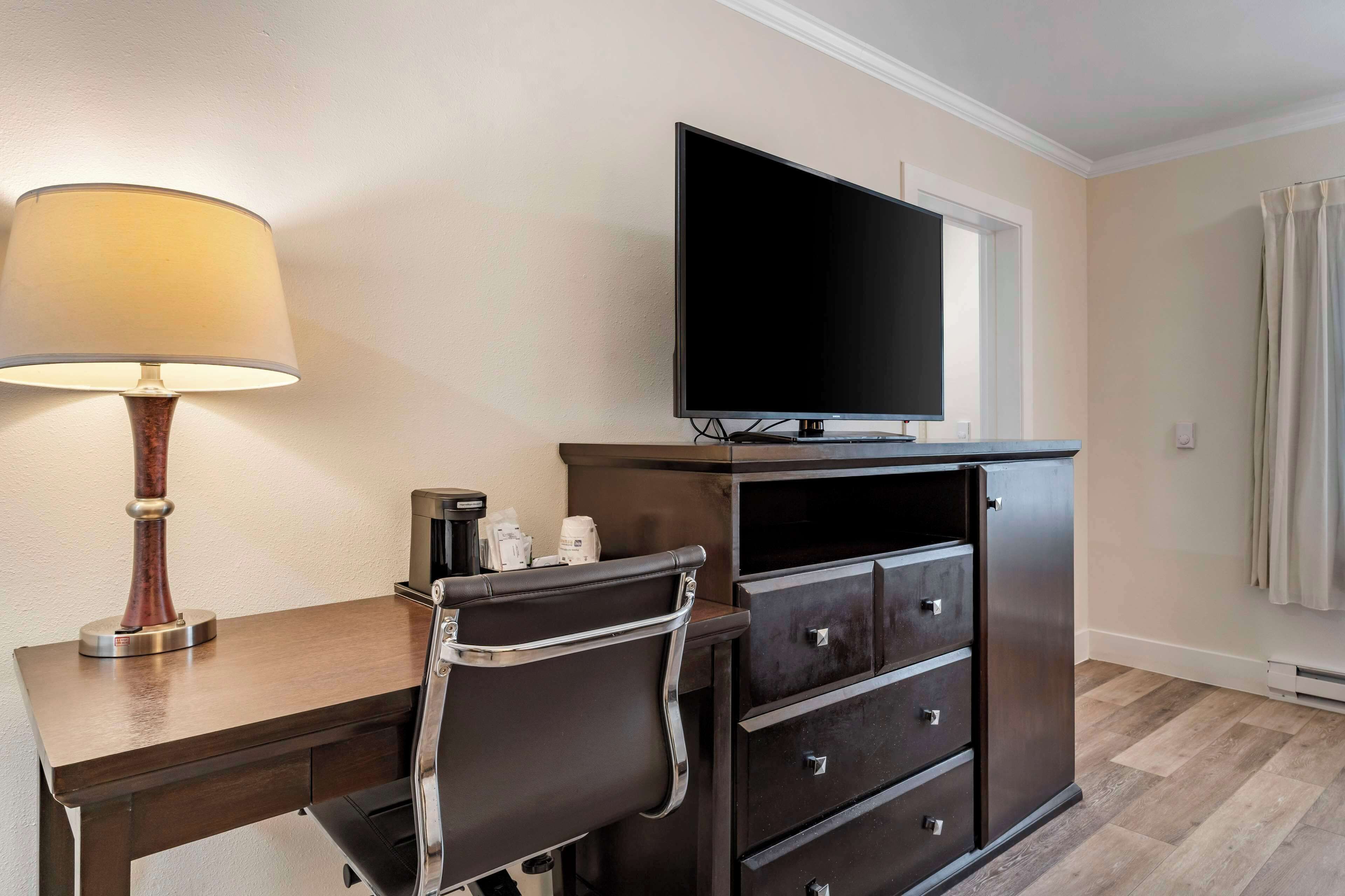 A hotel room with a desk, chair, television, and a cabinet with drawers.