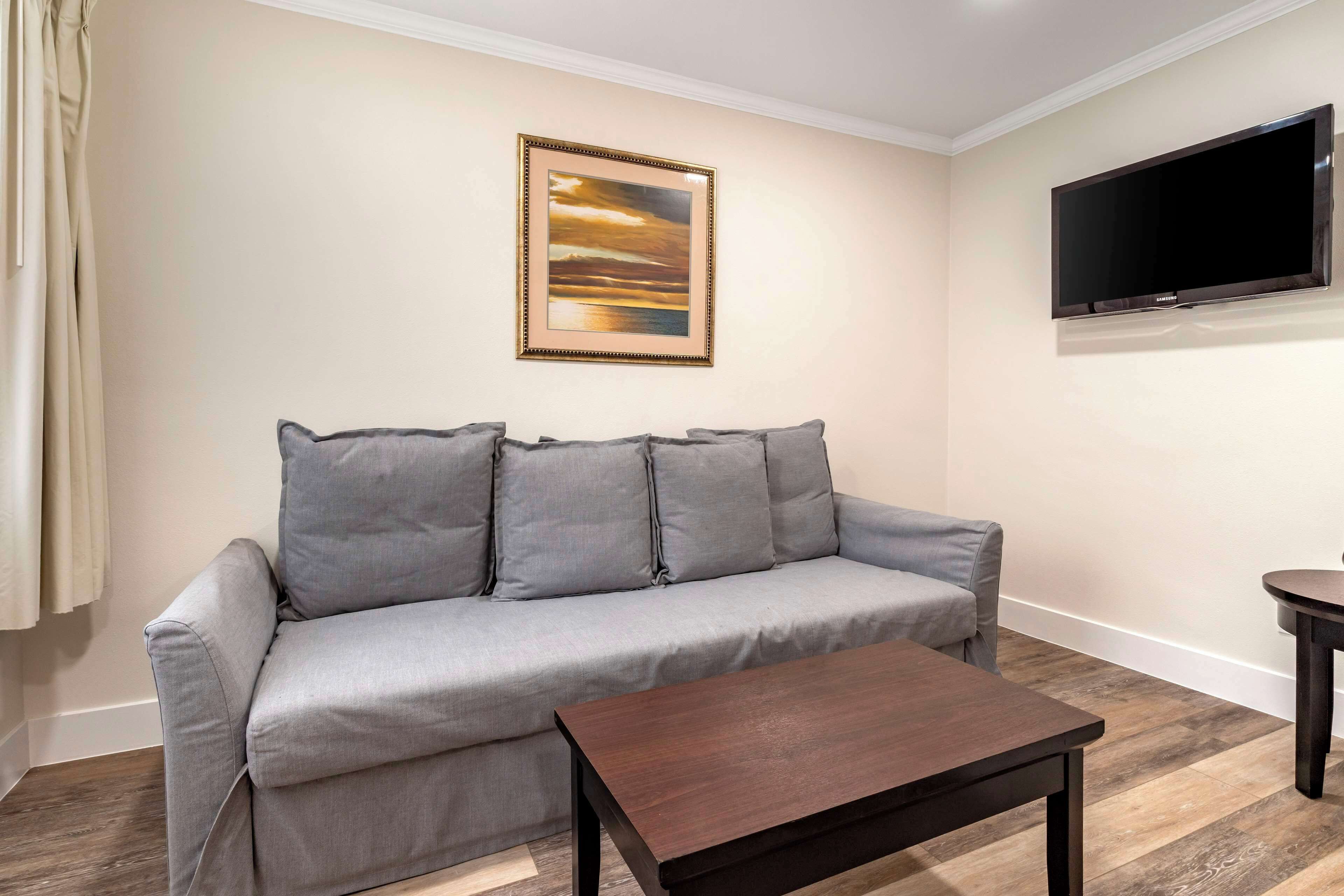 A living room with a grey sofa, a wooden coffee table, a framed picture on the wall, and a flat-screen TV.
