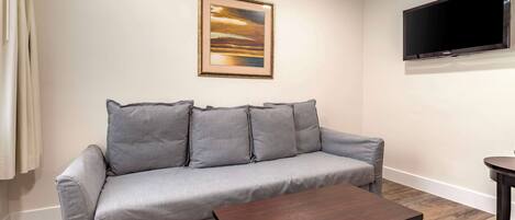 A living room with a grey sofa, a wooden coffee table, a framed picture on the wall, and a flat-screen TV.