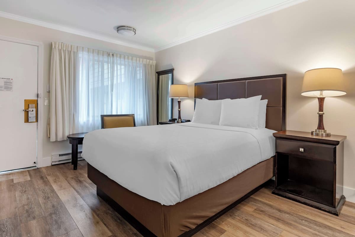 Ein Hotelzimmer mit einem großen Bett, zwei Nachttischen mit Lampen, einem Sessel und einem Fenster mit Vorhängen.