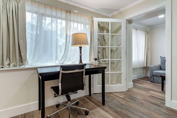 Une pièce comprenant un bureau, une chaise, une lampe et une fenêtre avec des rideaux, offrant une vue sur l’extérieur.