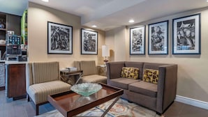Een moderne woonkamer met een bank, fauteuils, een koffieapparaat en ingelijste foto's aan de muur.