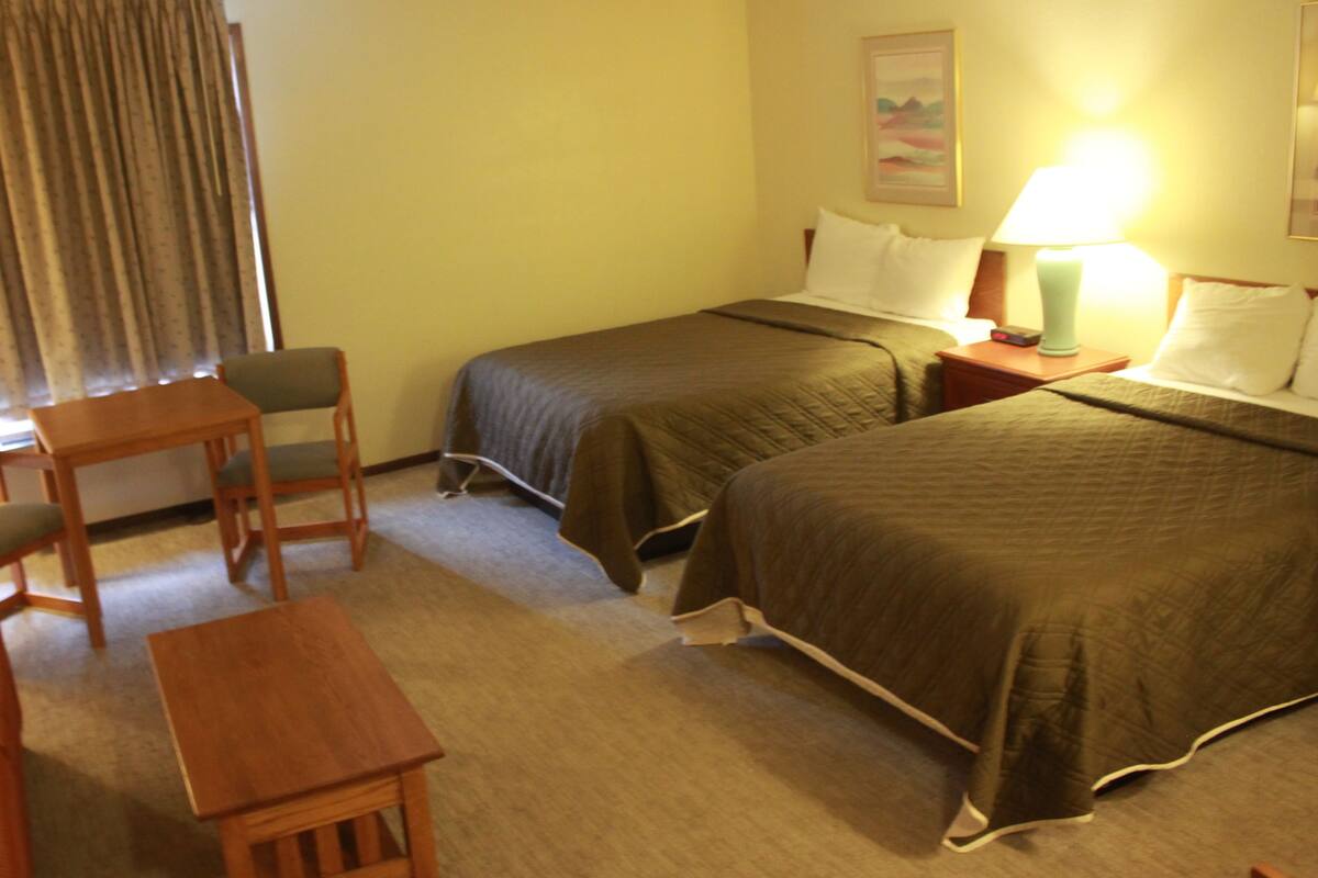 A hotel room with two single beds, a wooden desk, a chair, and a small table.