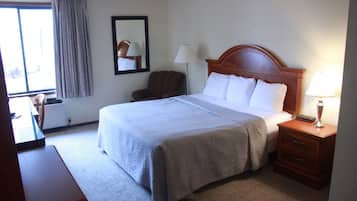 Ein Hotelzimmer mit einem großen Bett, einem hölzernen Kopfteil, einem Nachttisch mit Lampe, einem Sessel und einem Schreibtisch.
