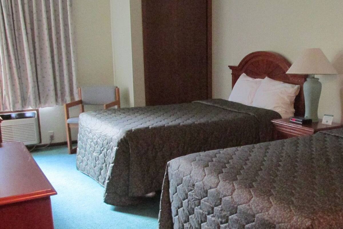 A hotel room with two beds, a desk, a chair, a lamp, and a window with curtains.
