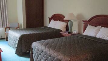 A hotel room with two beds, a desk, a chair, a lamp, and a window with curtains.