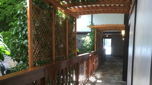 A covered walkway with a wooden railing, patterned carpet, and greenery on the sides. - Shawano Four Seasons Hotel (Shawano)