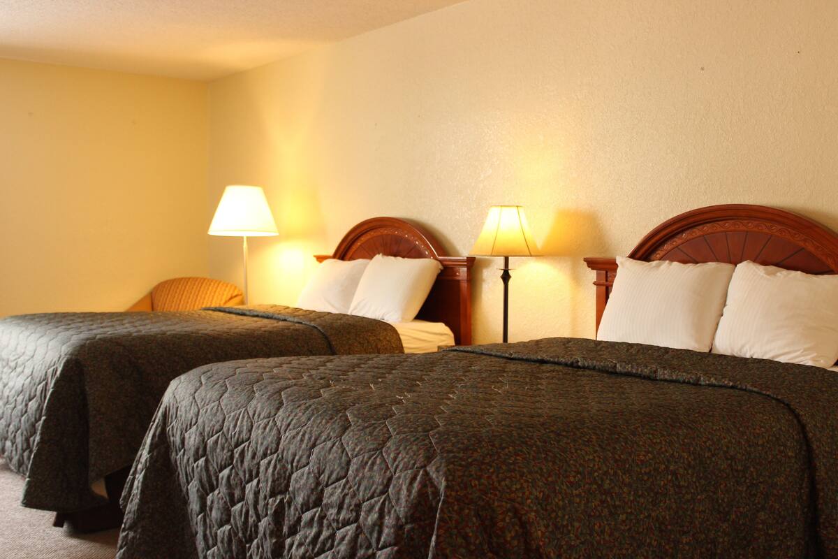 A hotel room with two beds, each with a wooden headboard and a lamp on either side.