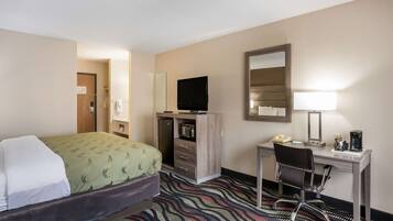 A hotel room with a bed, a desk with a chair, a television, a mirror, and a coffee maker.