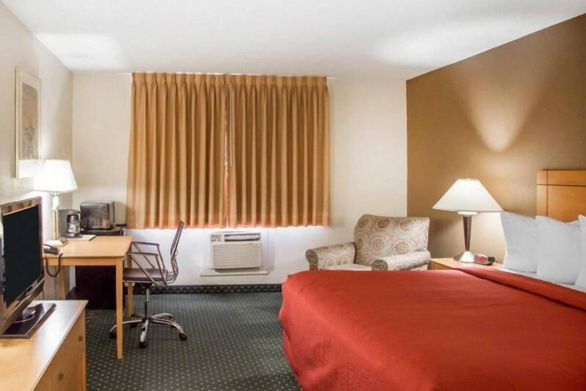 Ett hotellrum med en säng, ett skrivbord, en stol och ett fönster med gardiner.