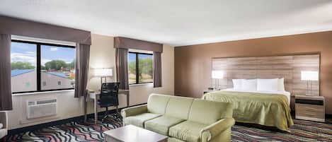 Habitación de hotel con cama, sofá verde, una mesita, escritorio y ventana con cortinas.