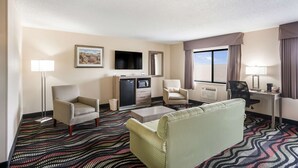 A hotel room with a sofa, armchairs, a desk, a flat-screen TV, a minibar, and a large window with curtains. - Quality Inn Cedar Rapids South (Cedar Rapids)