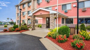 A multi-story hotel with a red facade, numbered 390, featuring a covered entrance, outdoor landscaping with red mulch and colorful flowers, and a clear blue sky. - Quality Inn Cedar Rapids South (Cedar Rapids)