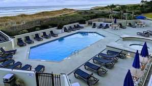 A pool area with lounge chairs and a view of the ocean.