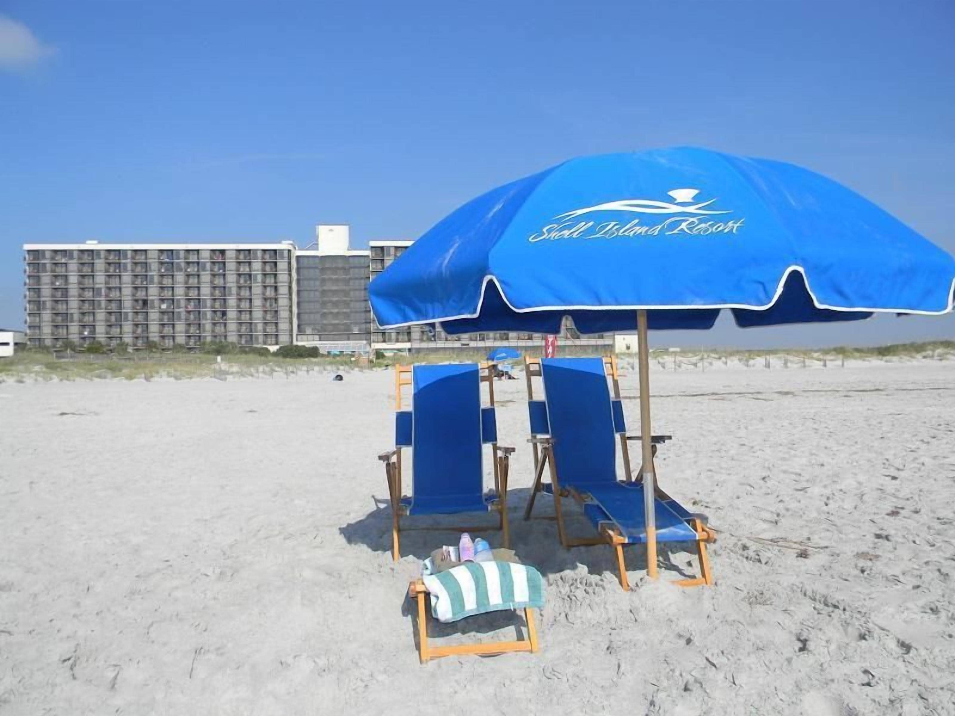 Ein Strandtuch mit dem Schriftzug "Shell Islands Resort", zwei blaue Strandstühle und ein kleiner Holzstuhl mit gestreiftem Handtuch.