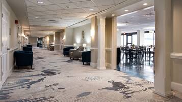 Un hall d’hôtel doté d’un tapis à motifs, d’espaces aménagés pour s’asseoir et d’un espace dédié à la restauration.