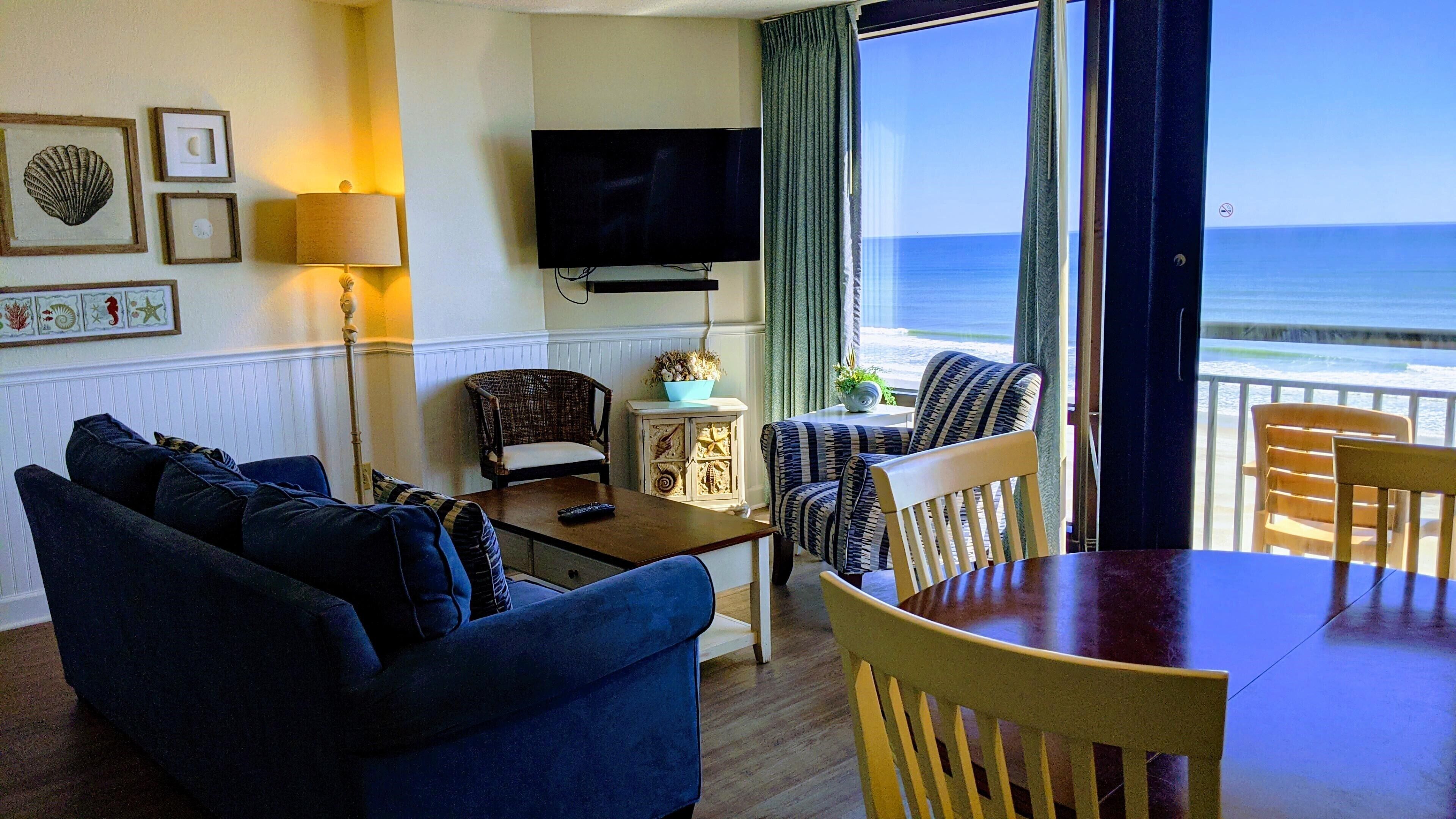 Un salon avec un canapé, des fauteuils, un téléviseur et une vue sur l’océan.