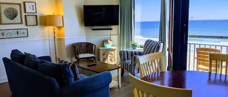 Un salon avec un canapé, des fauteuils, un téléviseur et une vue sur l’océan.