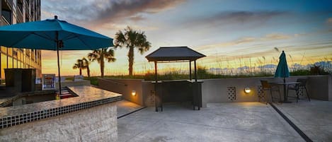 An outdoor patio area with a barbecue station, seating, and a view of the sunset.