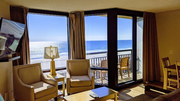 A hotel room with a large balcony, two armchairs, a small table, and a lamp.