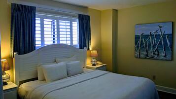 A hotel room with a bed, a nightstand with a lamp, a painting on the wall, and a window with curtains.