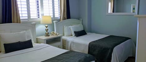 A hotel room with two beds, a nightstand with a lamp, a telephone, and a mirror on the wall.