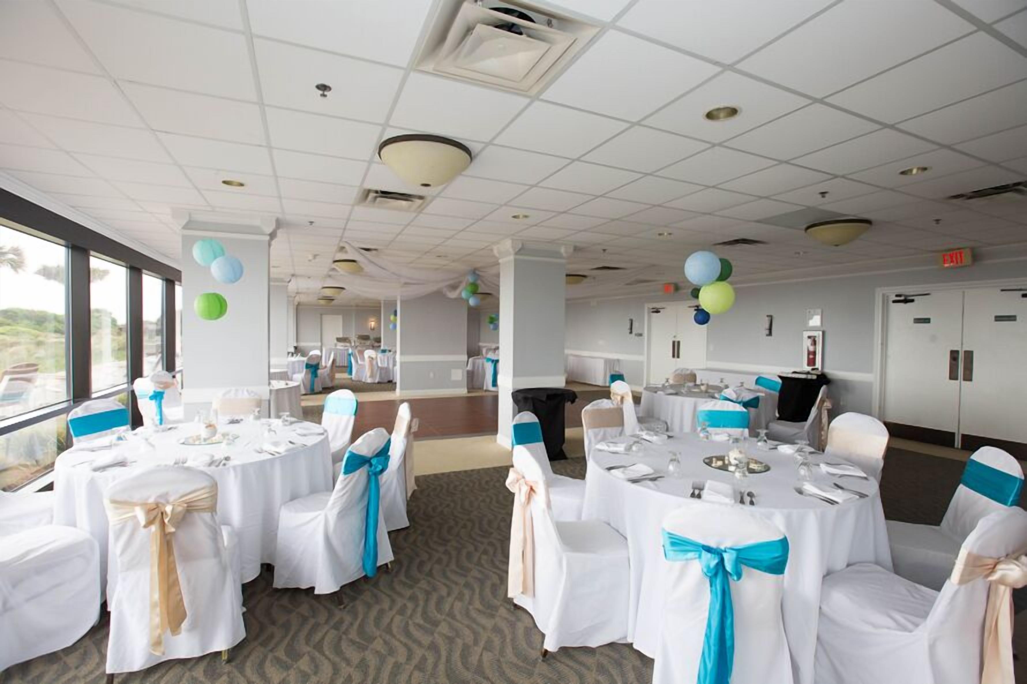 A banquet hall with round tables, white tablecloths, and chairs with blue sashes.