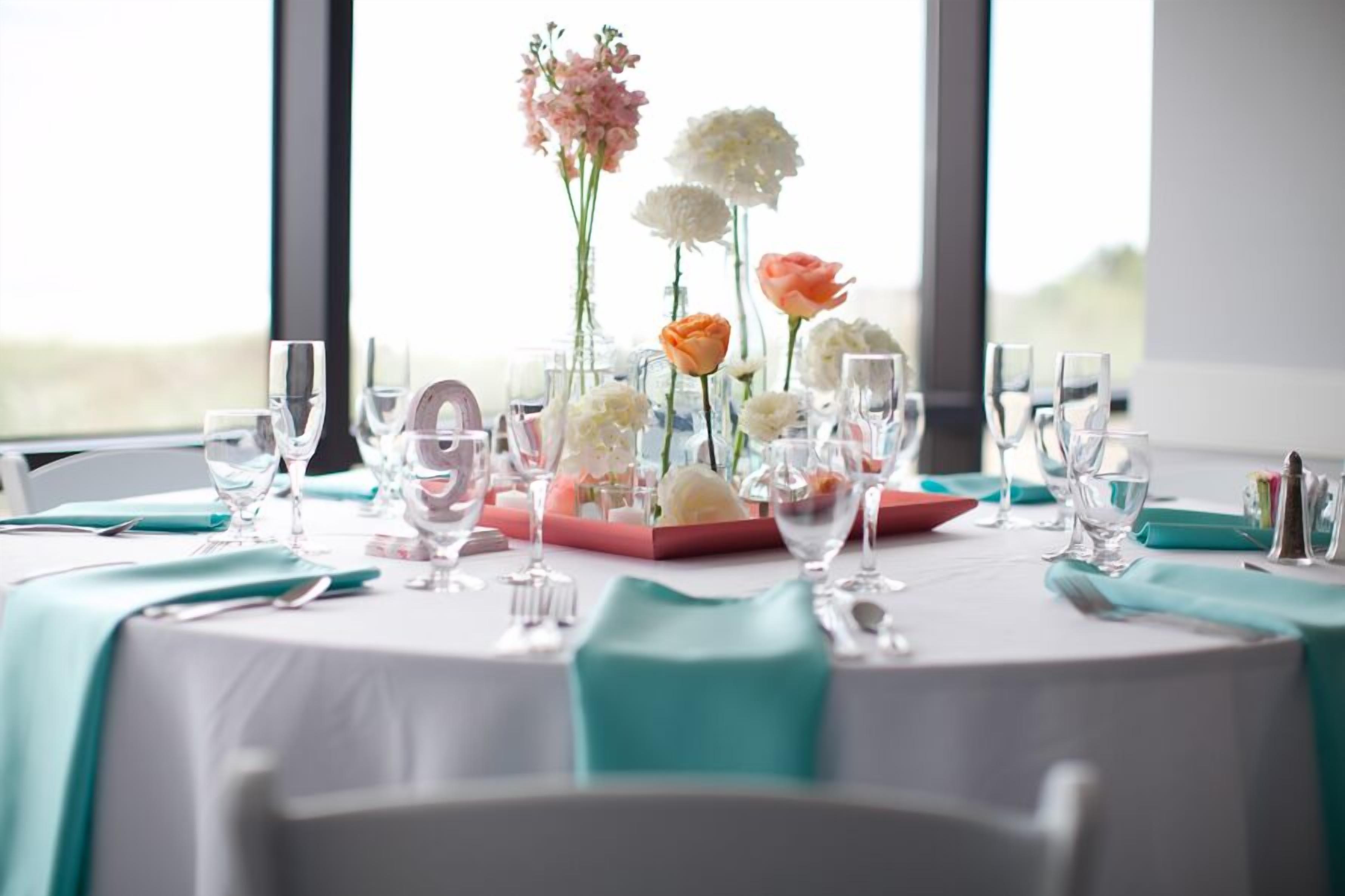 Une table dressée pour le repas, avec de beaux verres, un centre de table composé de fleurs et une nappe de couleur turquoise.