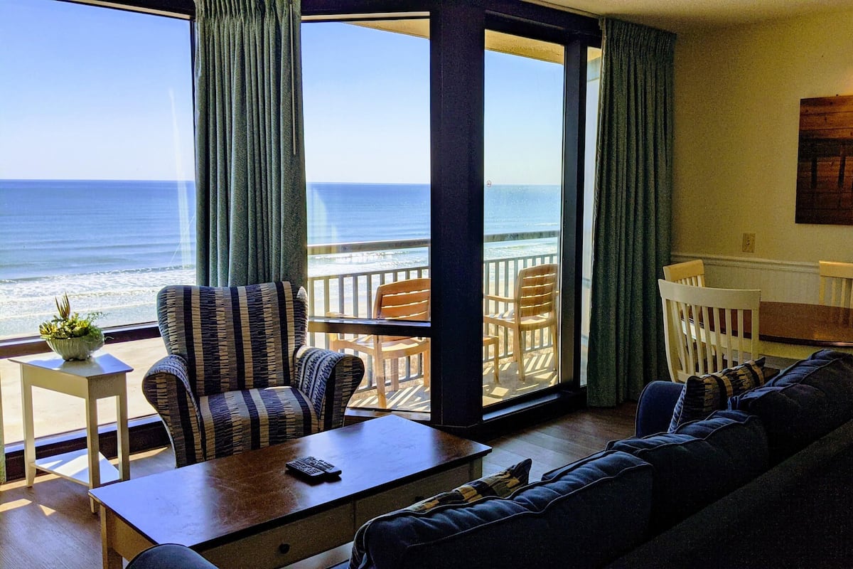 Ein Zimmer mit Meerblick, eine Couch, ein Esstisch mit Stühlen und ein kleiner Tisch mit einer Pflanze.