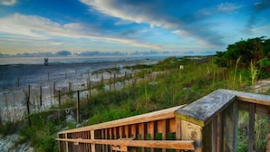 A wooden boardwalk leading to a beach with a fence and grassy dunes.