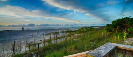 A wooden boardwalk leading to a beach with a fence and grassy dunes.