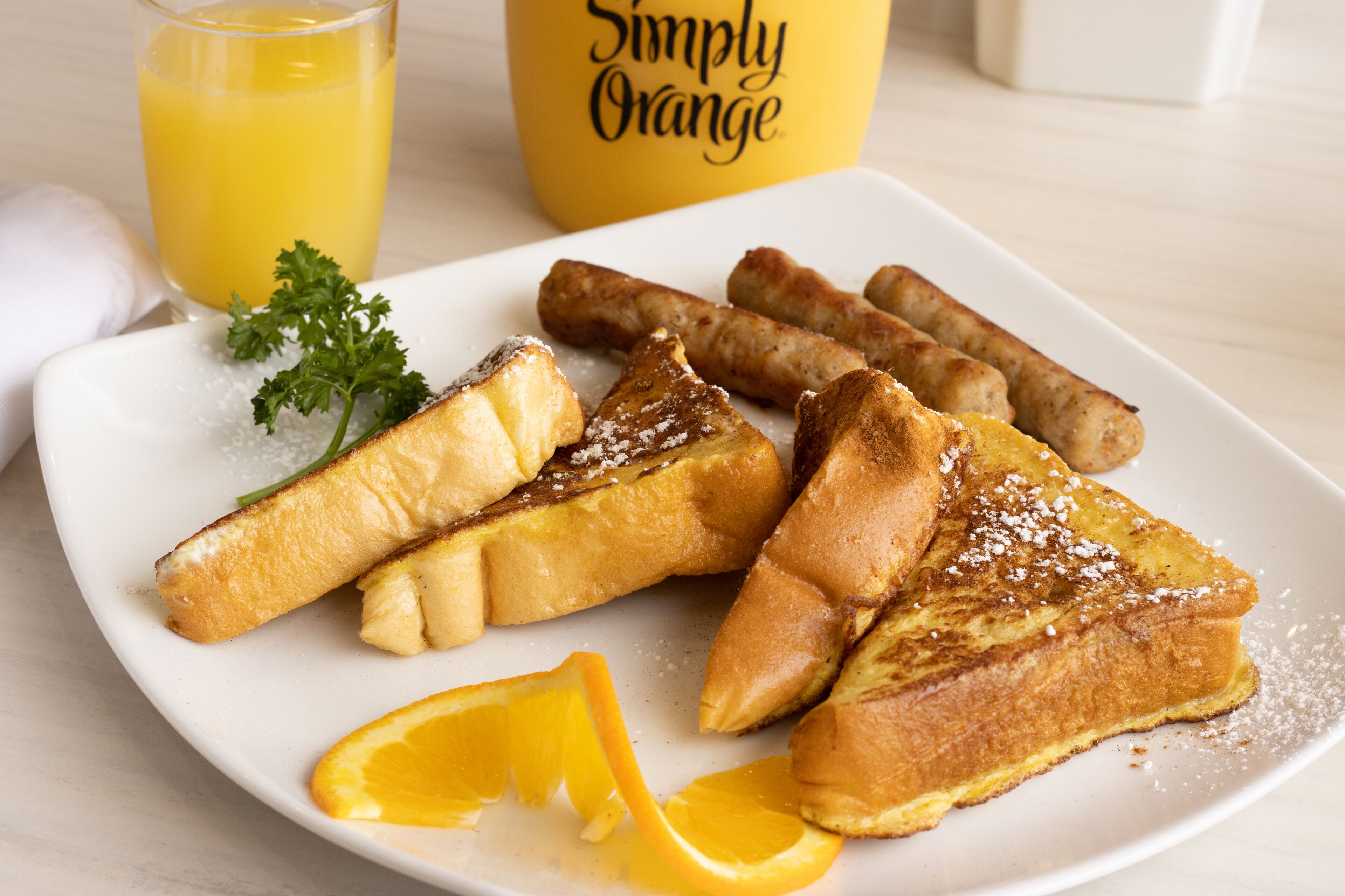 Une assiette de pain perdu saupoudré de sucre glace, accompagnée d’une tranche d’orange, le tout présenté sur une assiette blanche.