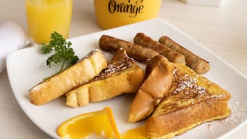 Une assiette de pain perdu saupoudré de sucre glace, accompagnée d’une tranche d’orange, le tout présenté sur une assiette blanche.