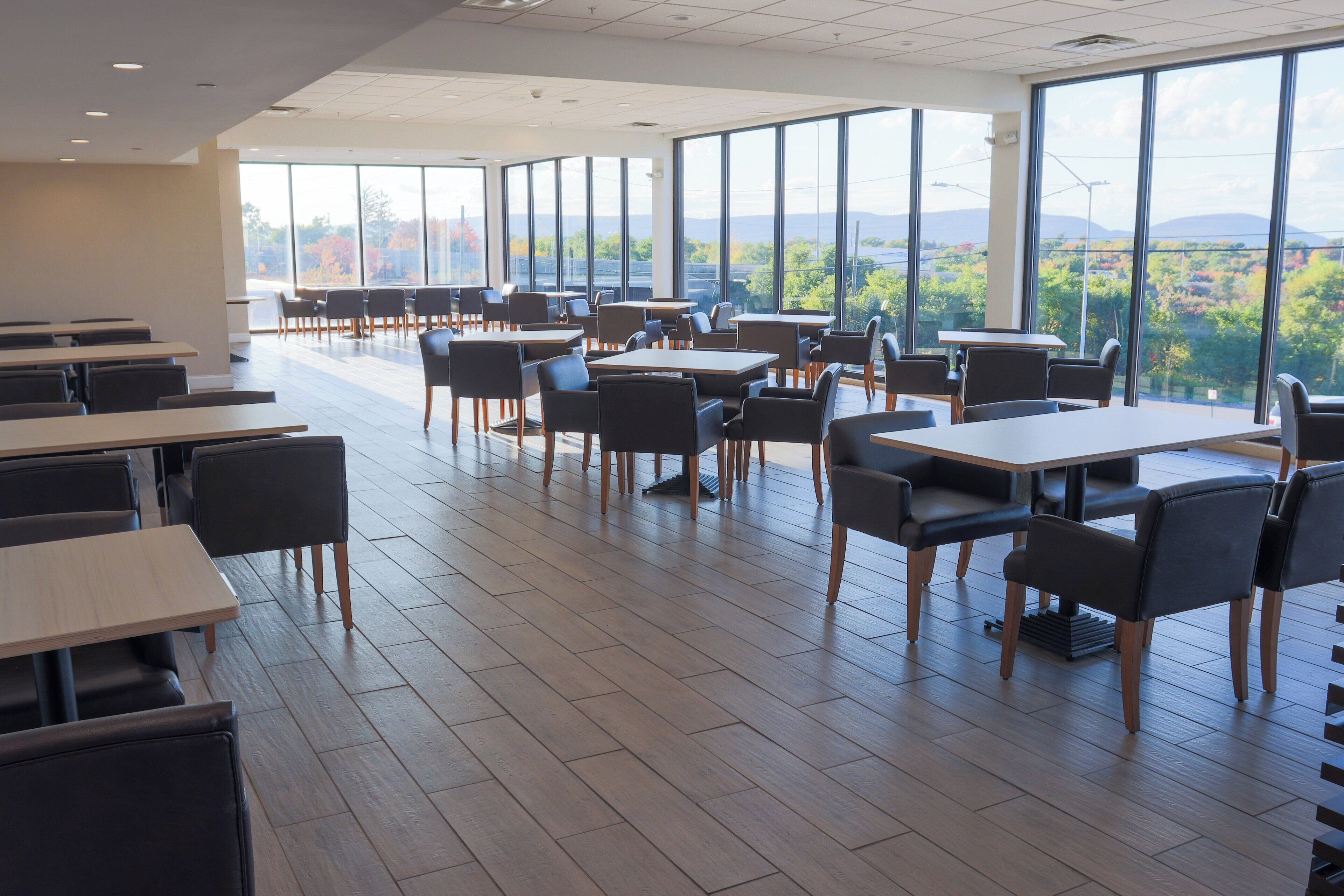 A spacious dining area with high tables and chairs, large windows offering a view of the outdoors.