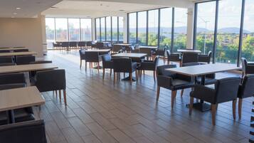 A spacious dining area with high tables and chairs, large windows offering a view of the outdoors.